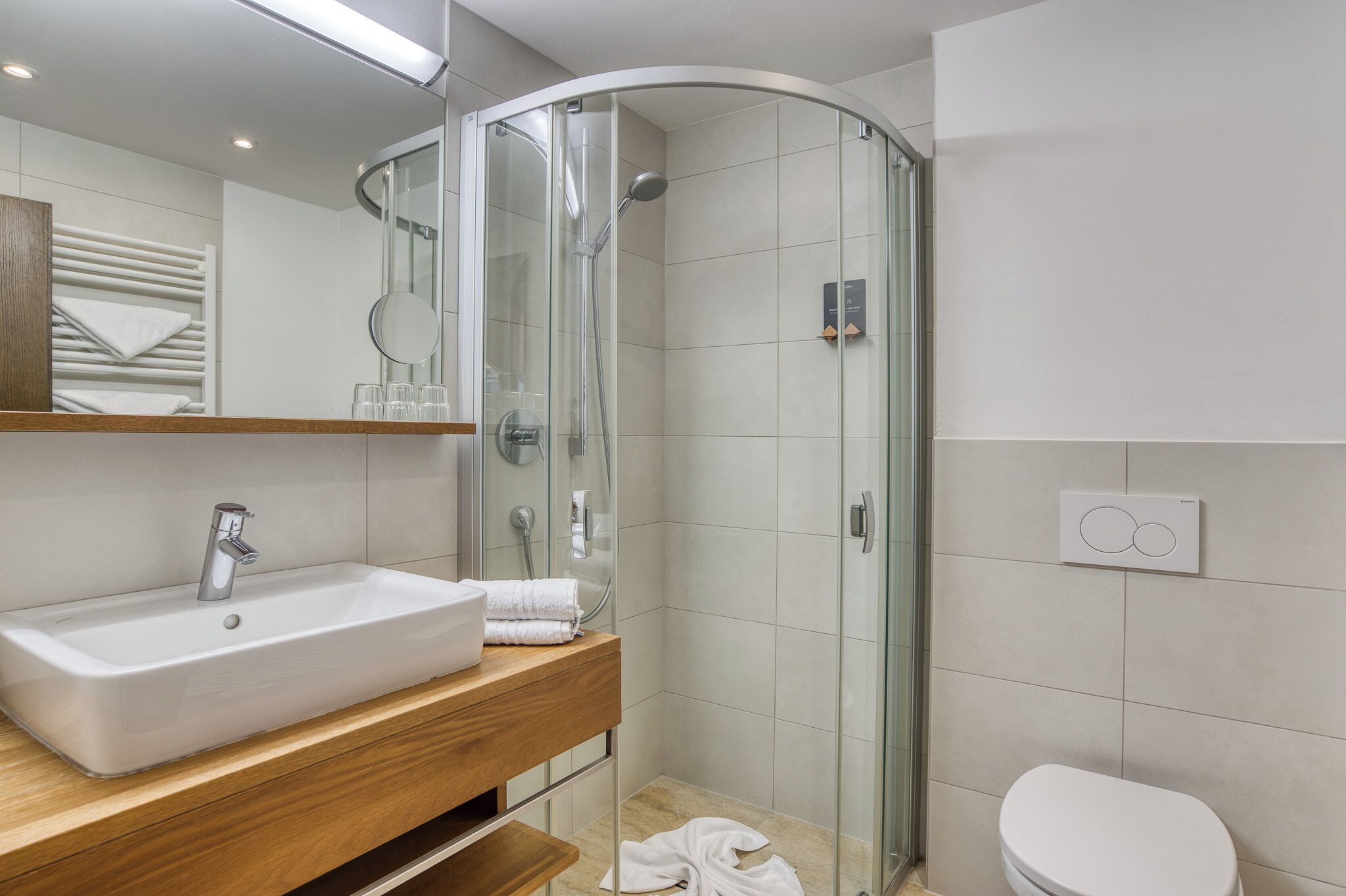 A modern bathroom with a curved glass shower enclosure, a wooden vanity with a sink, and a toilet.