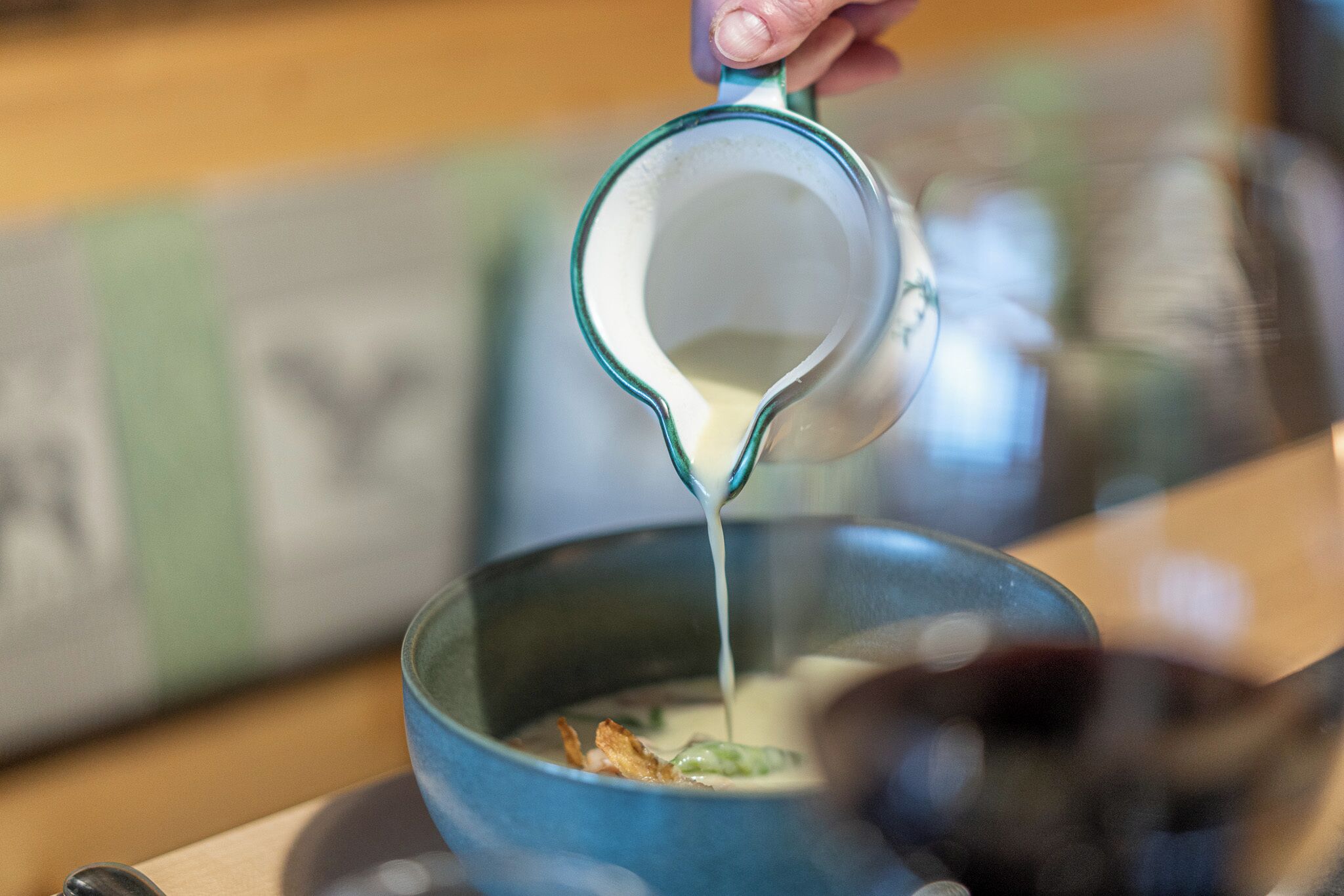 A hand pouring a white liquid into a blue bowl.
