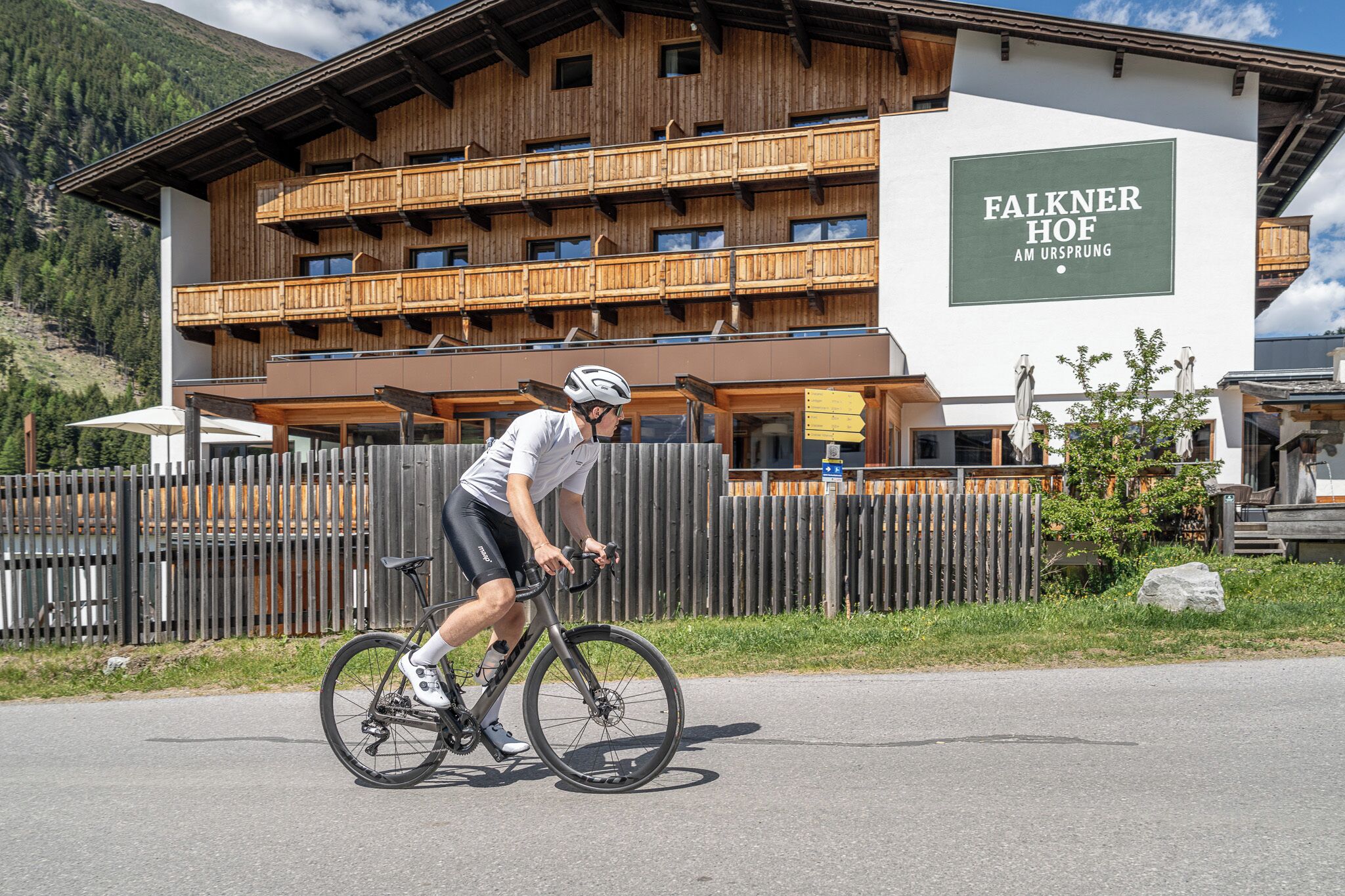A cyclist riding past a building with a sign reading 'Falkner Hof.'