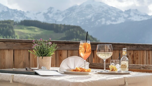 A table with a drink, a bottle, and a plate of food, set against a mountainous backdrop. - Hotel Falknerhof (Umhausen)