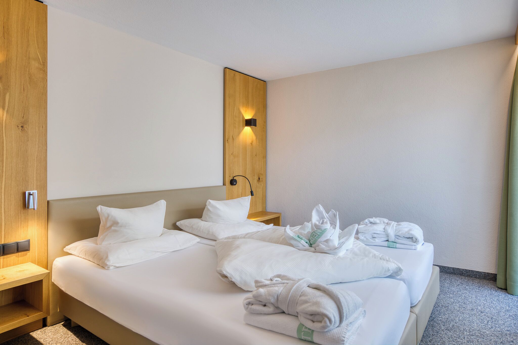A hotel room with a bed, a wooden headboard, a nightstand, and a wall-mounted light.