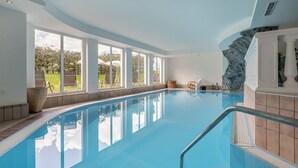 A swimming pool with a view of the outdoors, a stone wall, and a balcony with a railing. - Hotel Falknerhof (Umhausen)