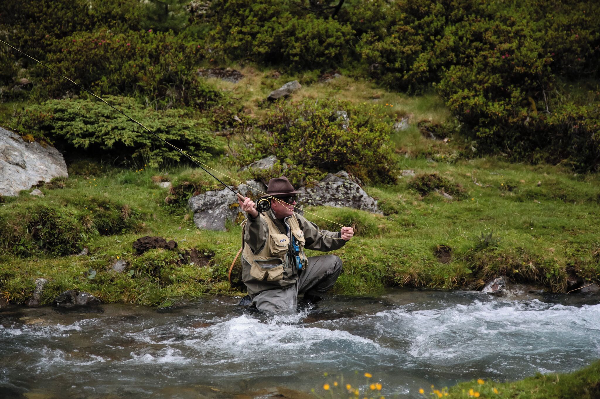 Una persona en un río, con sombrero y cargando una cámara.