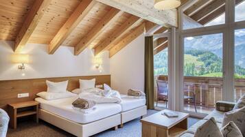 A room with a wooden ceiling, a bed, a sofa, and a balcony with a mountain view.