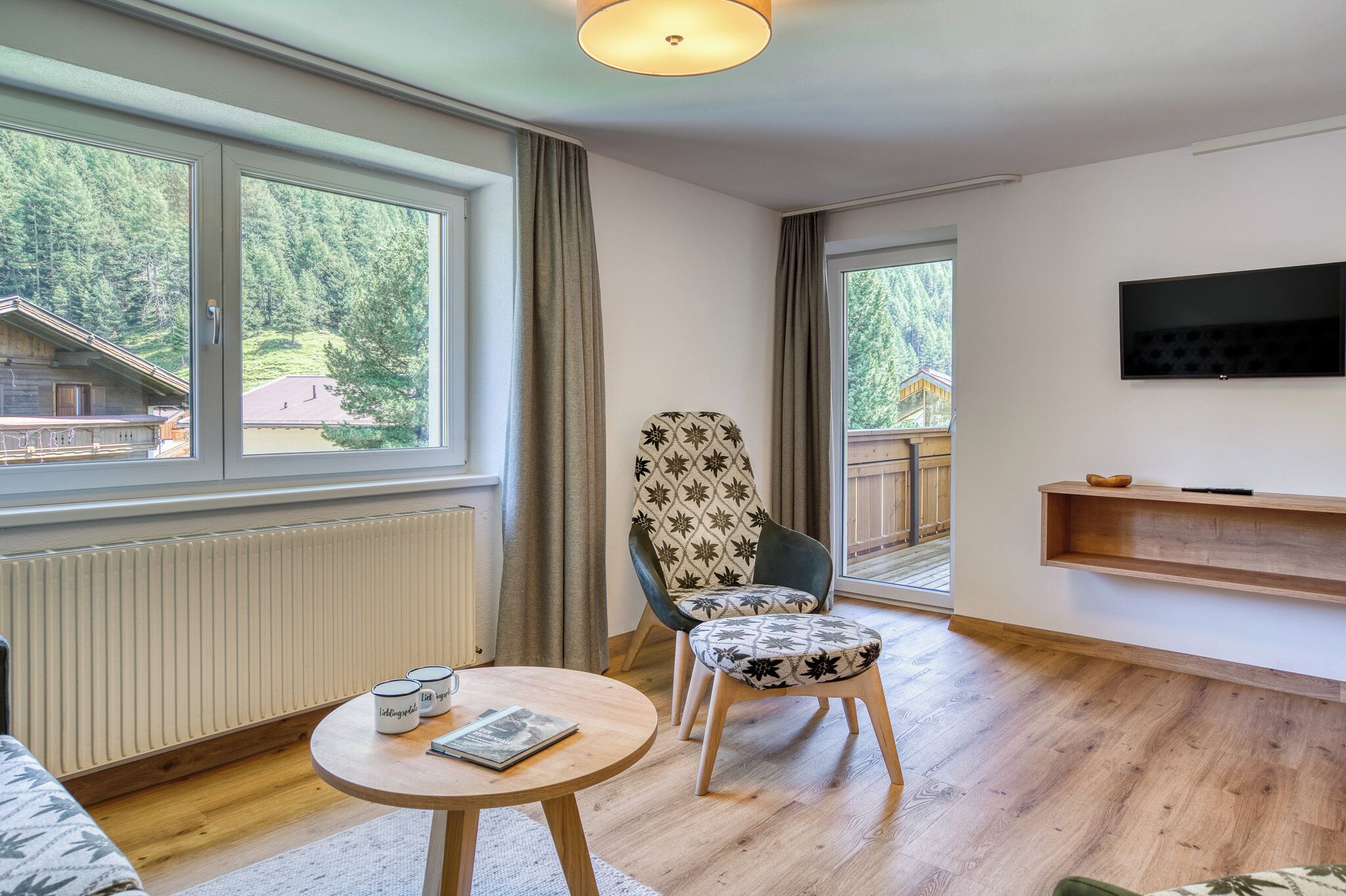 Una sala de estar moderna con un ventanal grande, un televisor, una mesa de madera y un sillón estampado.