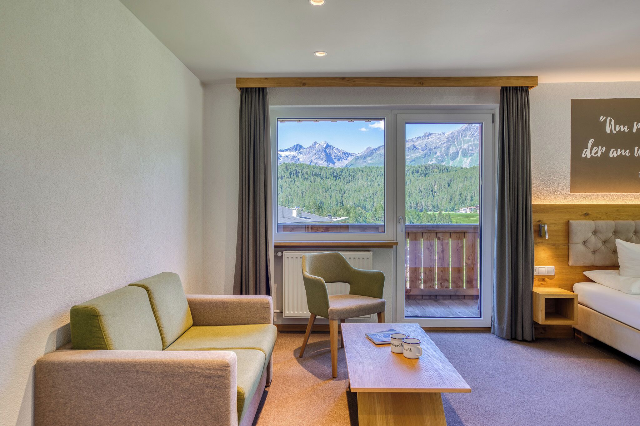 A modern hotel room with a sofa, armchair, and a table with a book and glasses.
