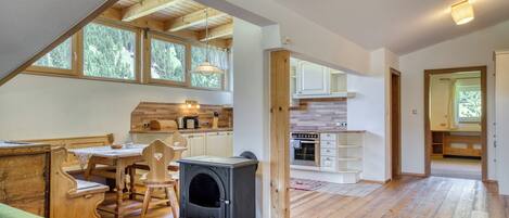 Amplia habitación estilo loft con una gran mesa de comedor de madera, un estufa de leña empotrada y una cocina con armarios blancos y encimera de madera.