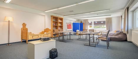 Una habitación con escritorio, sillas, estantería, un separador azul y una ventana con cortinas.