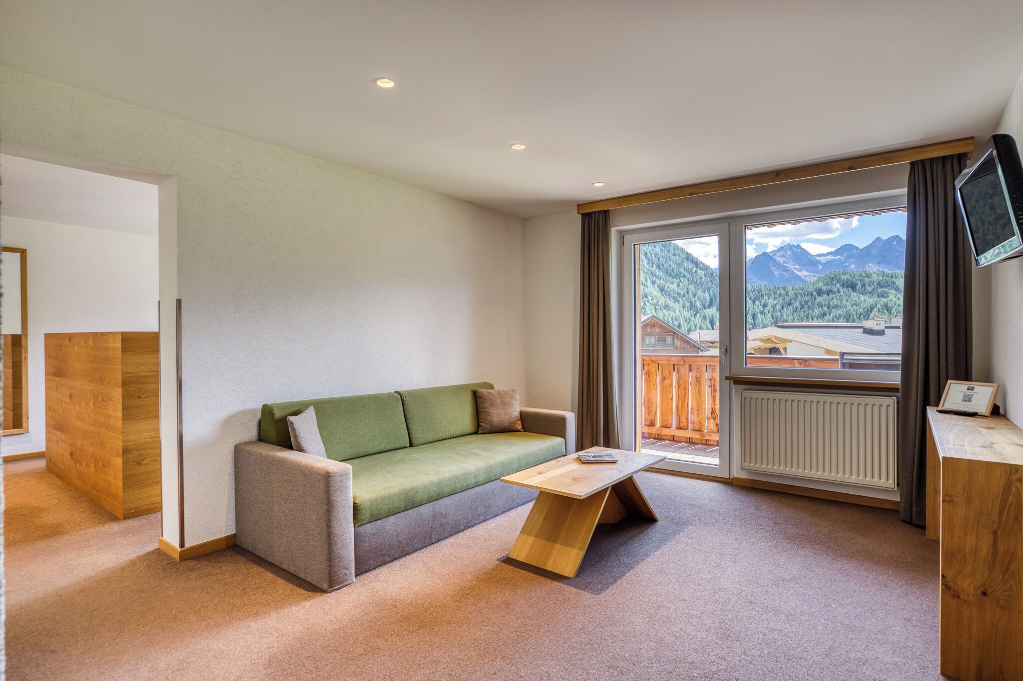 A modern room with a sofa, a wooden coffee table, and a view of mountains through a large window.