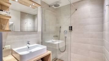 Un baño moderno con ducha envuelta en vidrio, un lavamanos blanco y un mueble de tocador de madera.