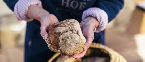 Eine Person hält ein Brot, trägt eine dunkle Schürze mit dem Aufdruck 'FALKNER HOF'.