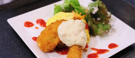 Un plato blanco rectangular con un alimento frito, una porción de salsa y una ensalada.