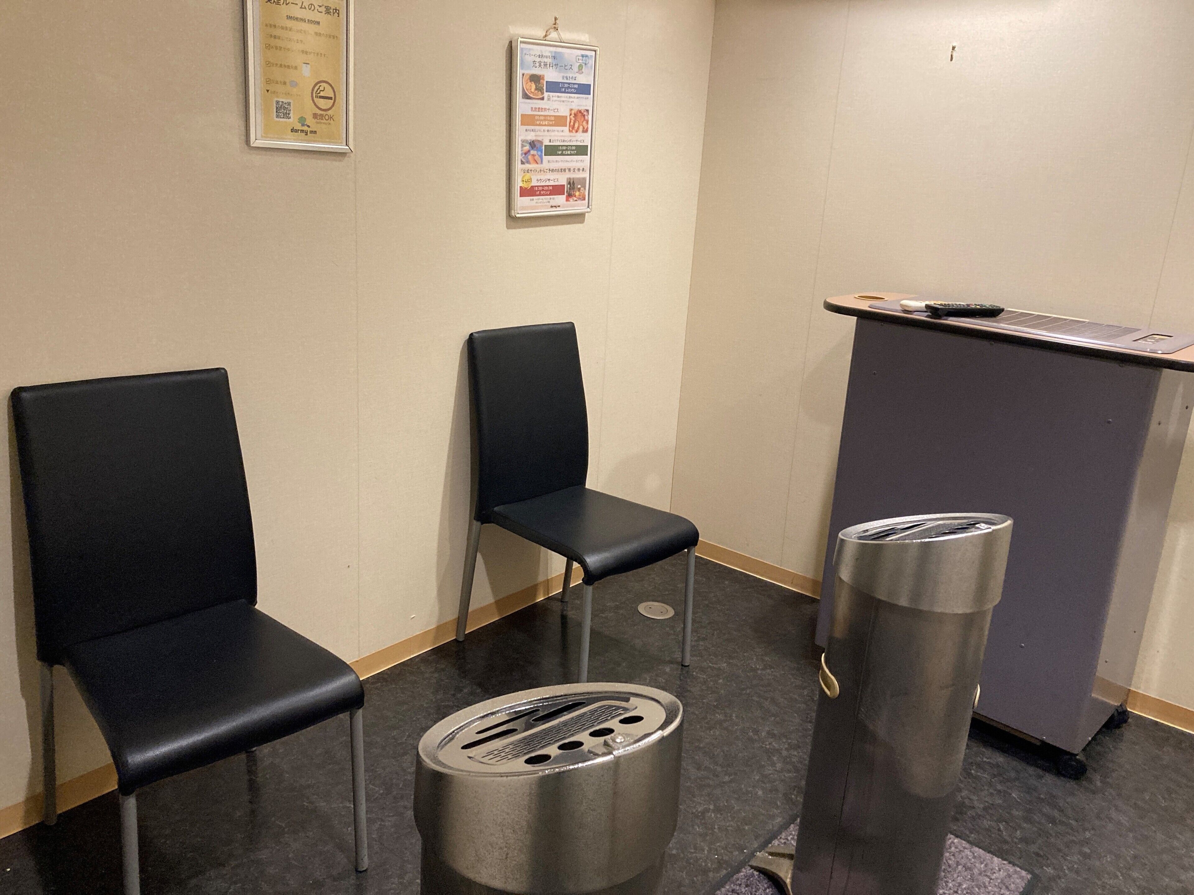 A waiting area with two black chairs, a small trash bin, and a desk with a keyboard and a remote control.