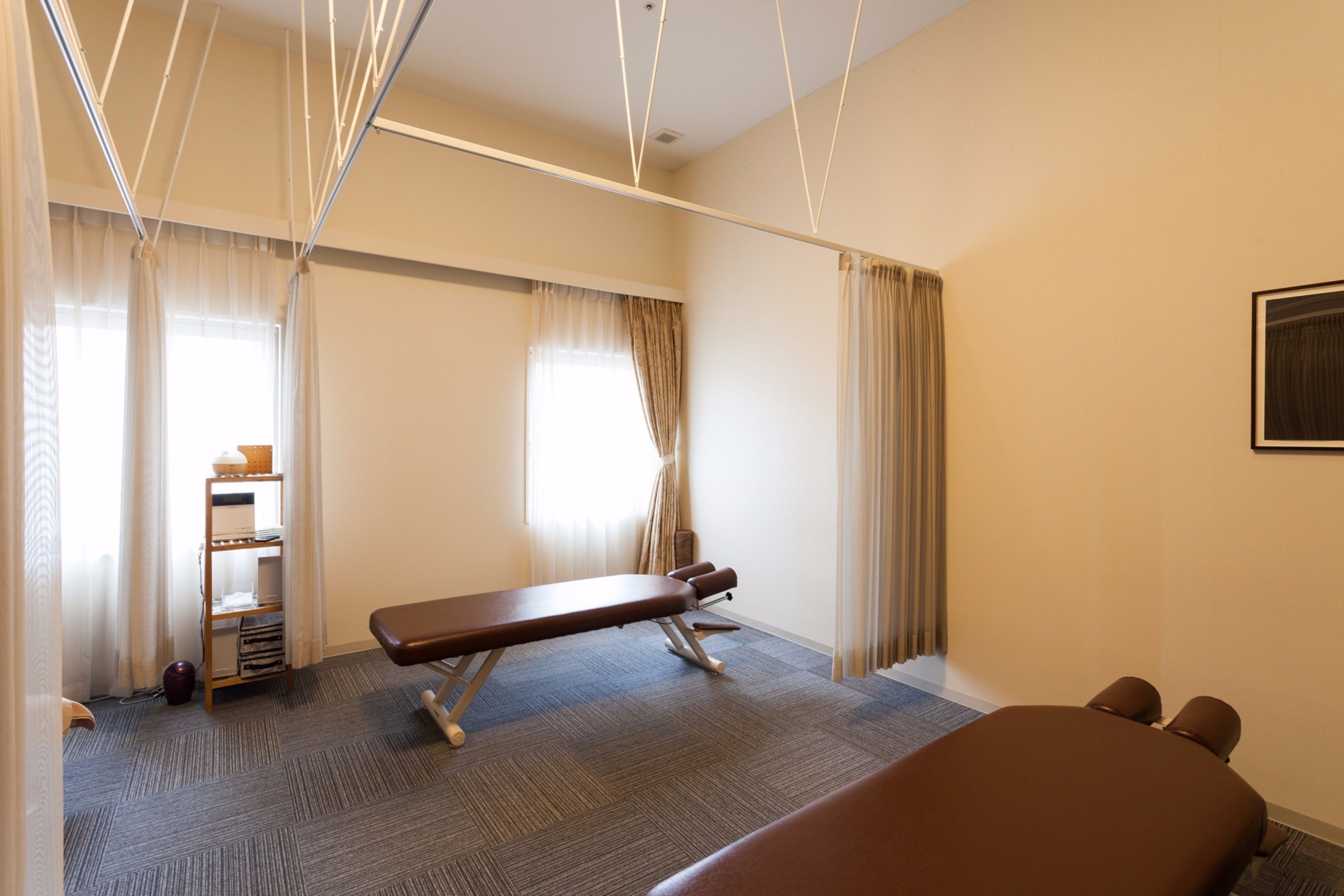 A room with a massage table, a shelf with towels, and a window with curtains.
