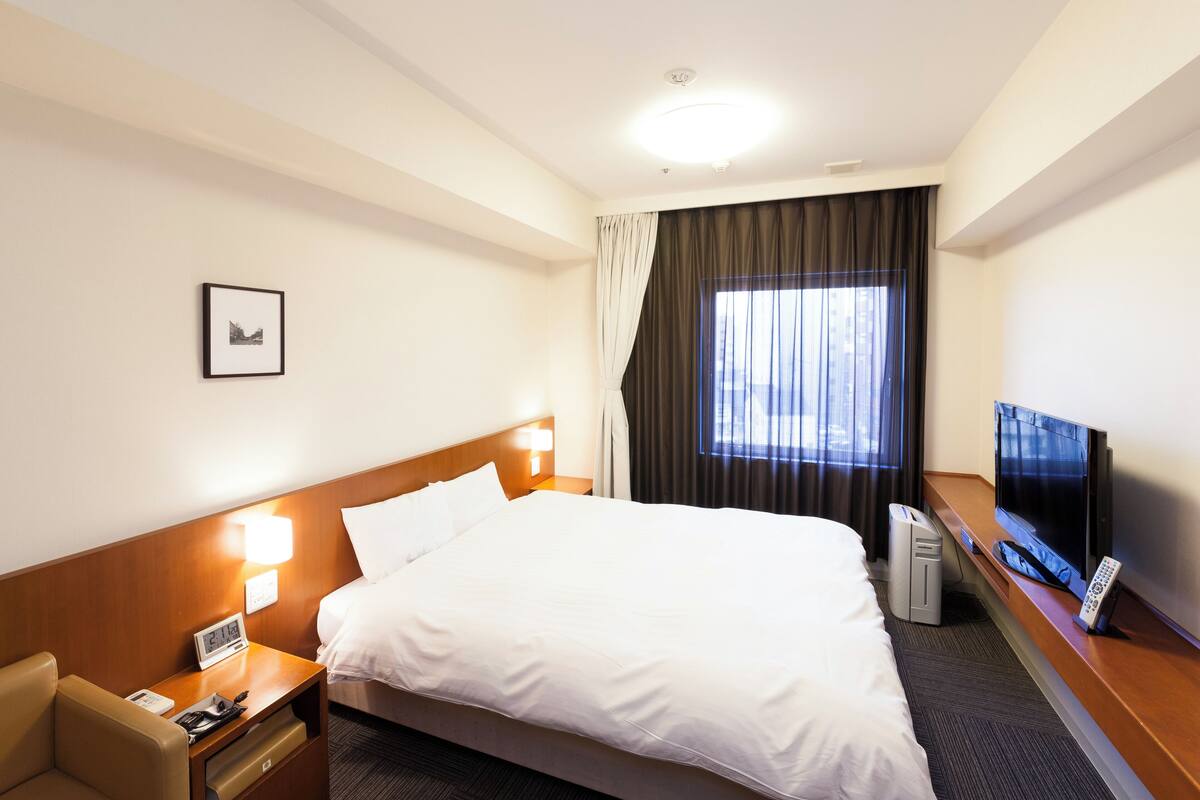 A hotel room with a large bed, bedside tables with lamps, a TV, and a desk.