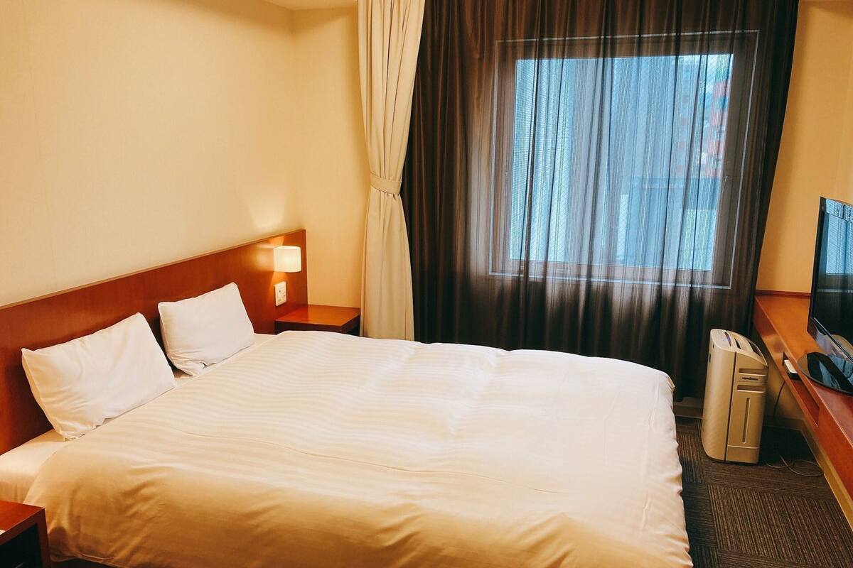 A hotel room with a large bed, a TV, a desk with a computer, and a window with curtains.