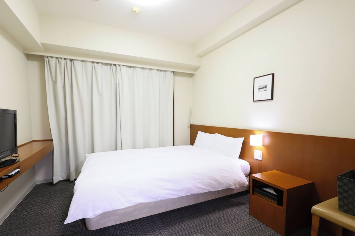 A hotel room with a bed, a TV on a stand, a bedside table, and a nightstand.