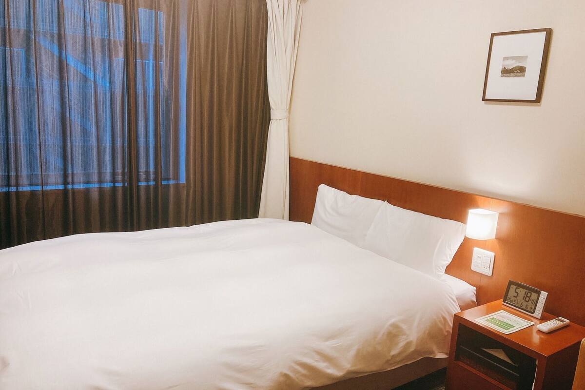 A hotel room with a bed, a nightstand with a clock, a lamp, and a framed picture on the wall.