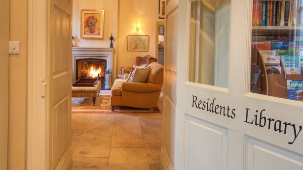 A cozy living room with a fireplace, a sofa, and a bookshelf filled with books. - The Collingwood Arms Hotel (Cornhill on Tweed)