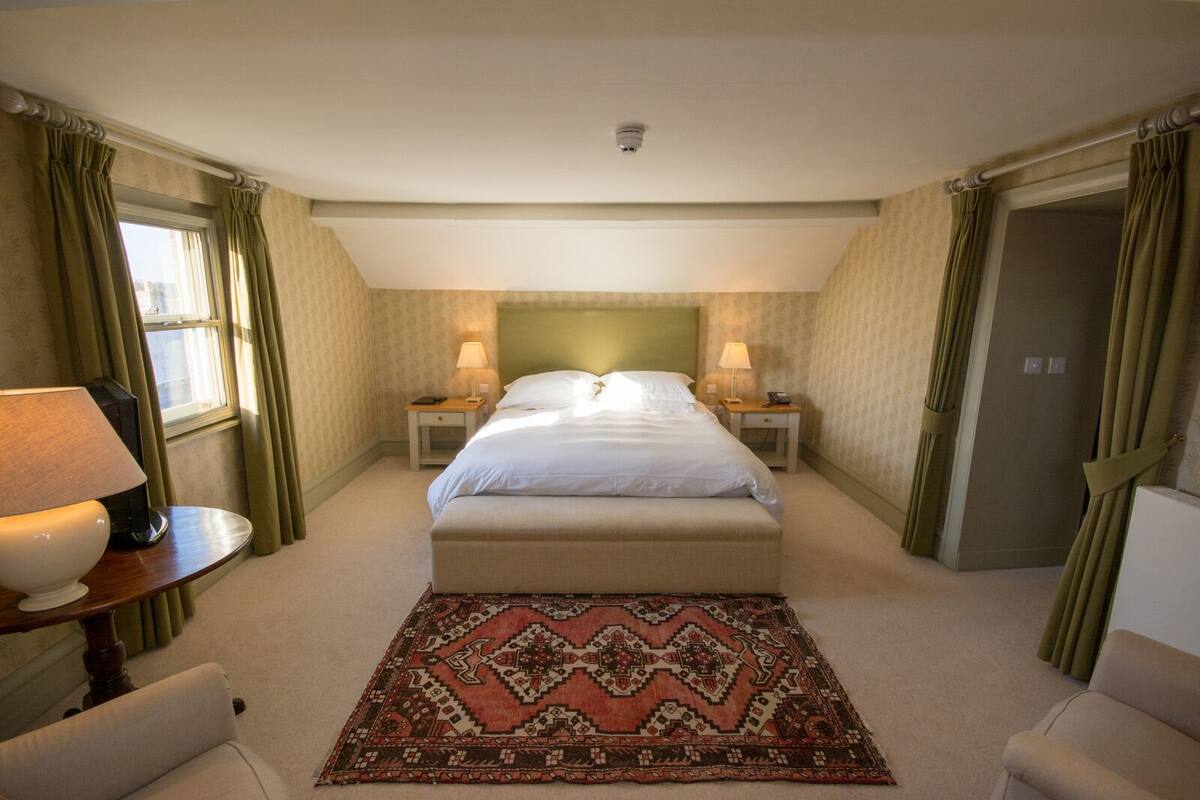 A hotel room with a large bed, two bedside tables with lamps, a patterned rug, and green curtains.