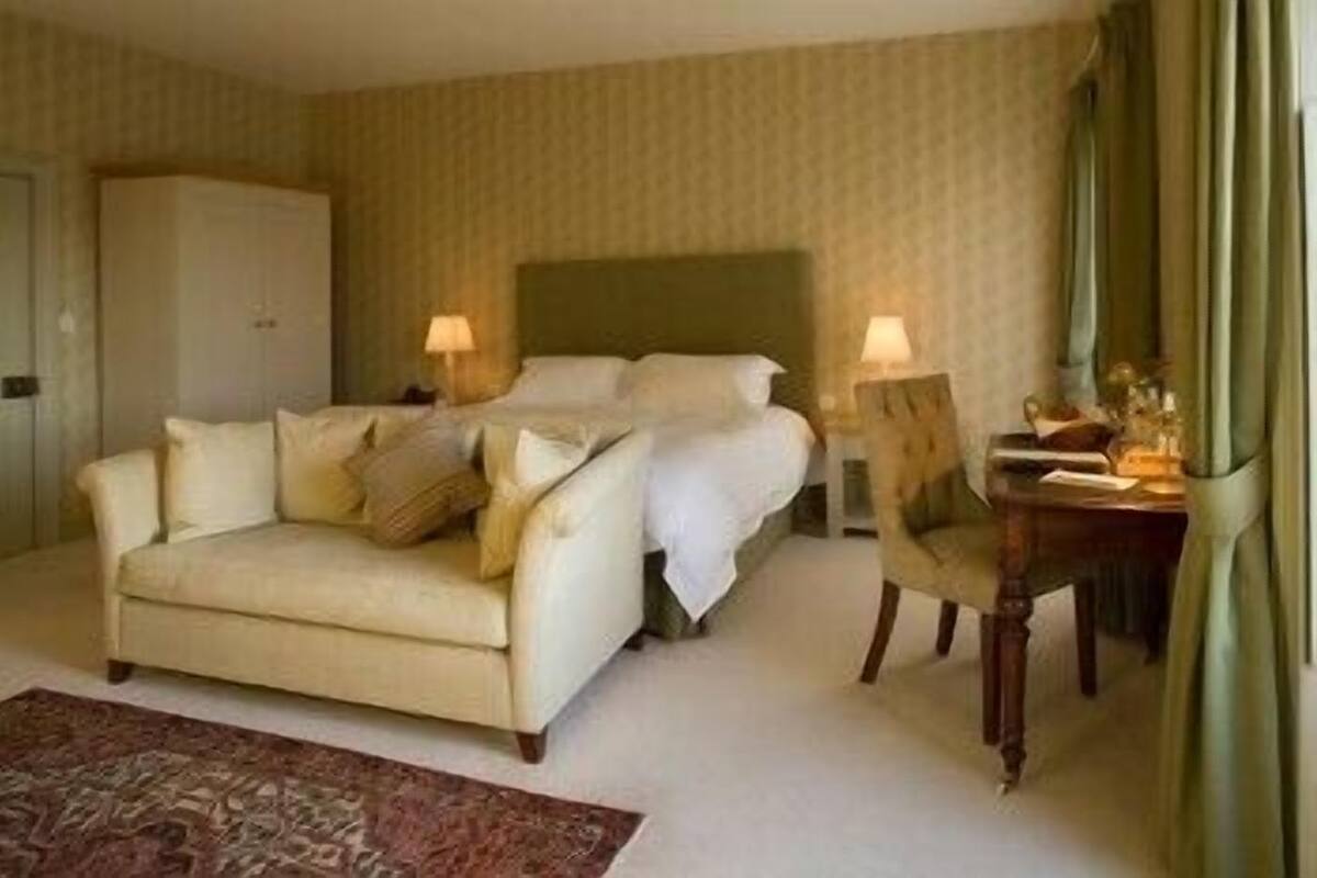 A hotel room with a bed, a sofa, a desk with a lamp, and a chair.