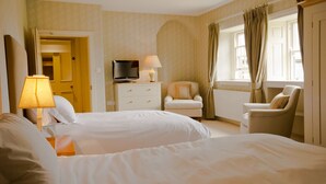 A hotel room with two beds, a TV, a lamp, a chair, and a window with curtains. - The Collingwood Arms Hotel (Cornhill on Tweed)