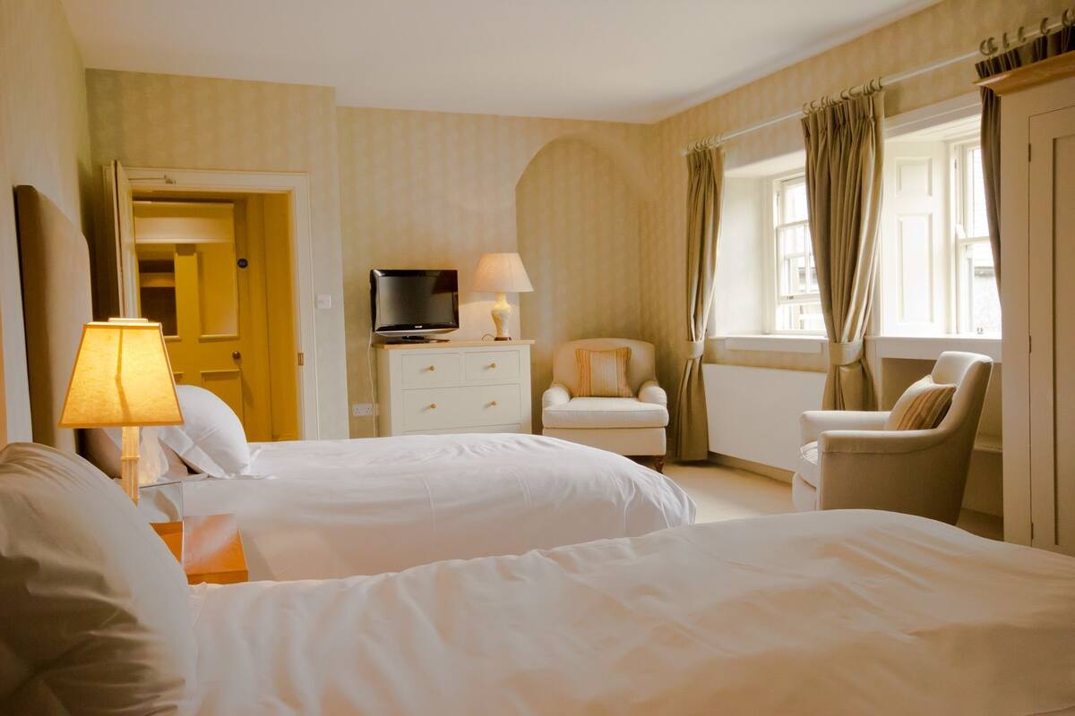 A hotel room with two beds, a TV, a lamp, a chair, and a window with curtains.