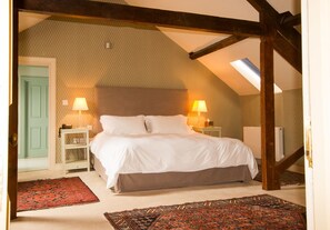 A bedroom with a sloped ceiling, a bed with white bedding, two bedside lamps, a small nightstand, and a red patterned rug.