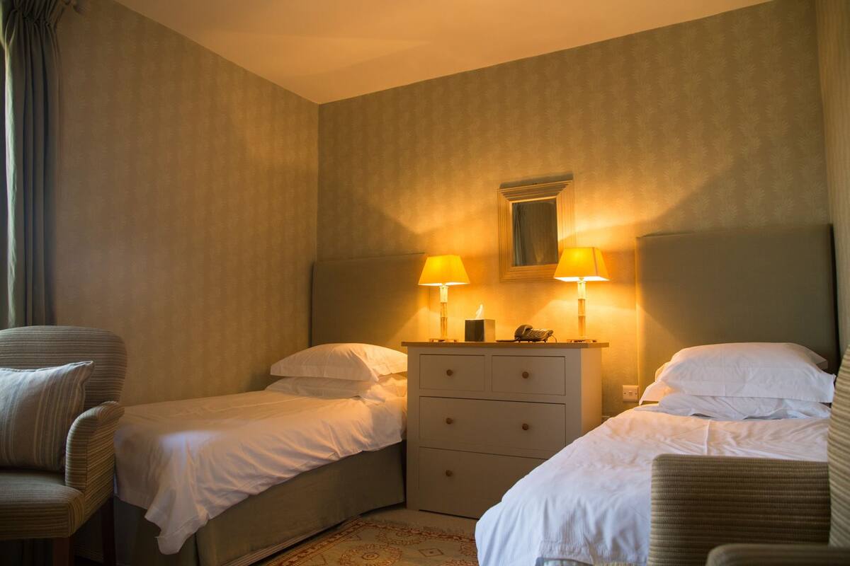 A hotel room with two single beds, a dresser with drawers, two bedside lamps, and a mirror above the dresser.