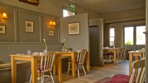 A dining area with wooden tables and chairs, framed pictures on the walls, and a patterned rug on the floor. - The Collingwood Arms Hotel (Cornhill on Tweed)
