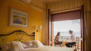 Quarto de hotel com uma cama, um quadro na parede e uma varanda com mesa e cadeiras.