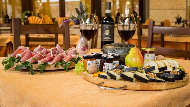 Tábua de frios com diversos embutidos, queijos, frutas e nozes, acompanhada por duas taças de vinho tinto e uma garrafa de vinho.