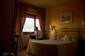 Ein Hotelzimmer mit einem Bett, einem Schreibtisch mit einem Laptop, einem Stuhl und einem Fenster mit Vorhängen.