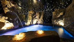 Um spa com hidromassagem rodeado por formações rochosas e um teto com luzes penduradas.