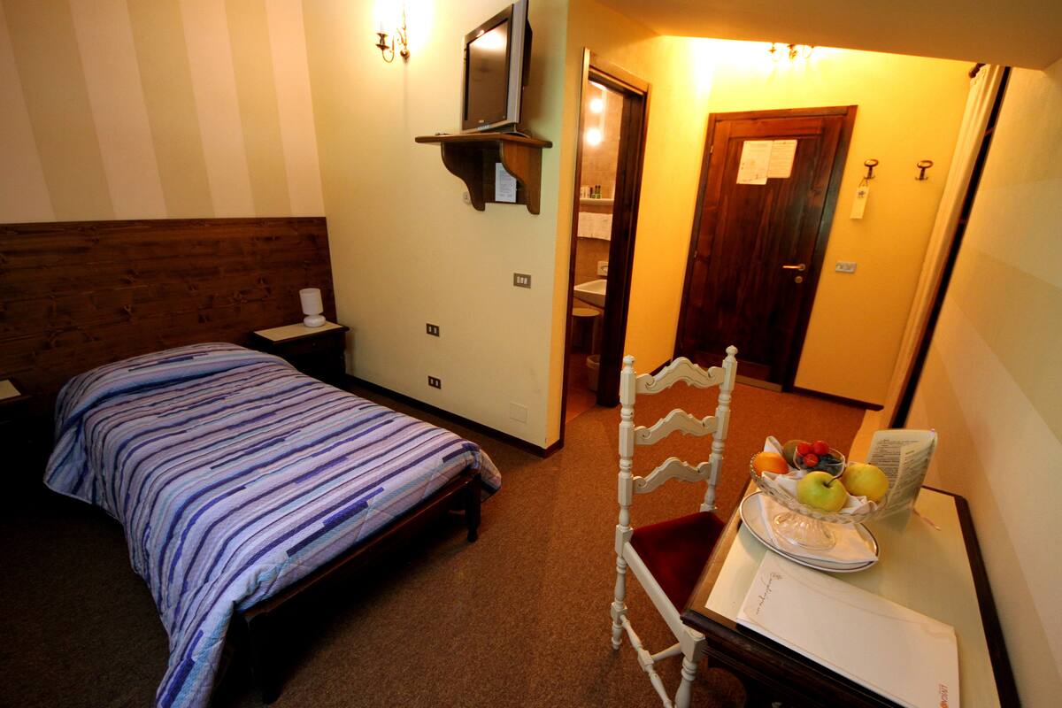 A hotel room with a bed, a chair, a table with a fruit basket, and a mirror on the wall.