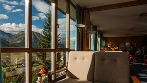 A room with large windows, a sofa, a table with a vase and a mug, and a view of mountains. - Hotel Parè (Livigno)