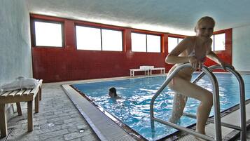 Ein Innenpool mit gefliestem Boden, einer Sitzbank und einer Person an der Poolleiter.