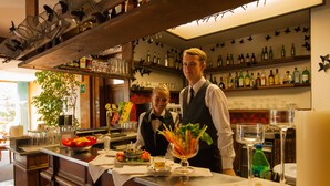 A bar area with a counter, shelves with bottles, and a decorative ceiling. - Hotel Parè (Livigno)