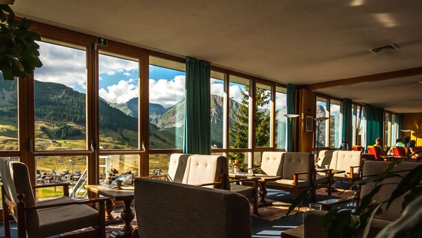 A room with large windows offering a mountain view, several chairs, a table, and a lamp. - Hotel Parè (Livigno)
