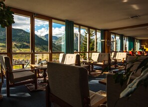 Une pièce dotée de grandes fenêtres donnant sur les montagnes, de plusieurs chaises, d’une table et d’une lampe.