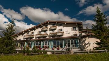 Ein Hotel mit mehreren Balkonen, im Hintergrund eine Skipiste und ein klarer Himmel.