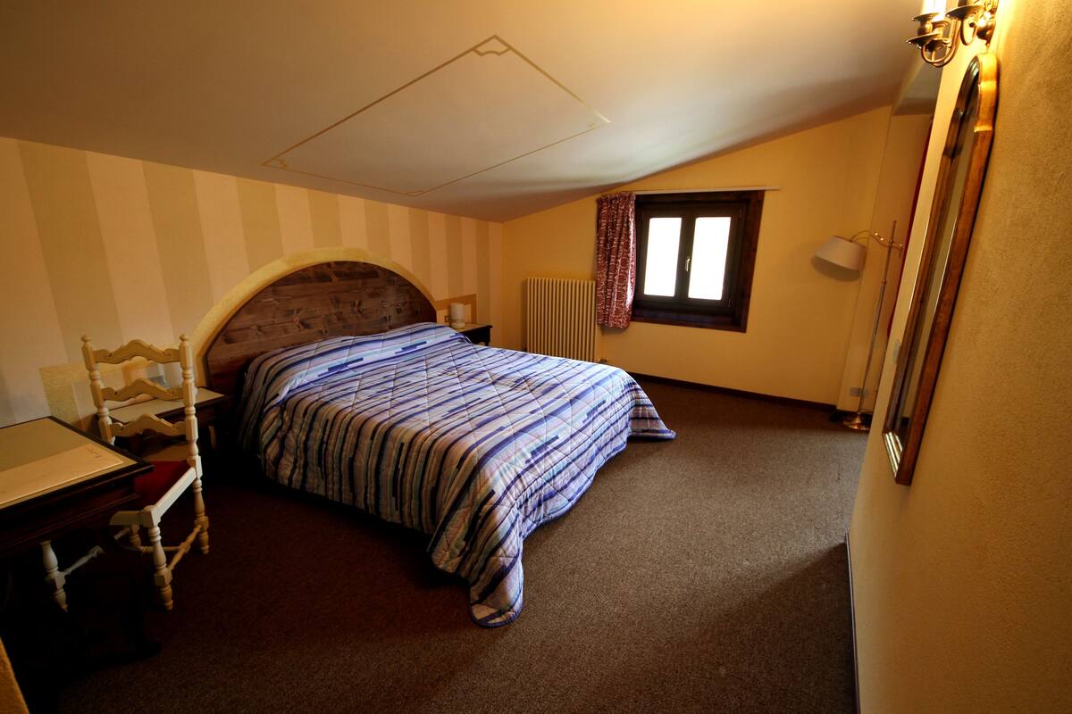 A bedroom with a bed, a chair, a desk, a radiator, and a window with curtains.