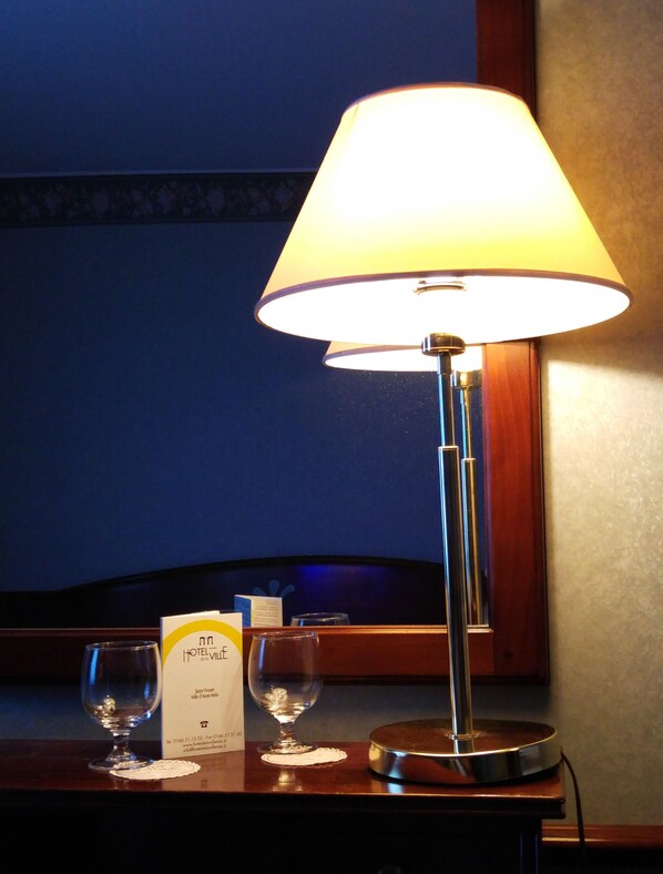 A hotel room with a table lamp, two empty wine glasses, and a hotel sign.