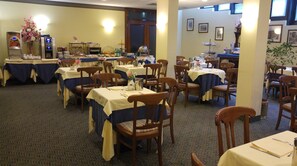 A dining area with multiple tables and chairs, a buffet station, and a wall with framed pictures.