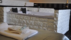 A bathroom with a stone wall, a white bathtub, a black towel, and a bottle of champagne. - Navona Nice Room (Rome)