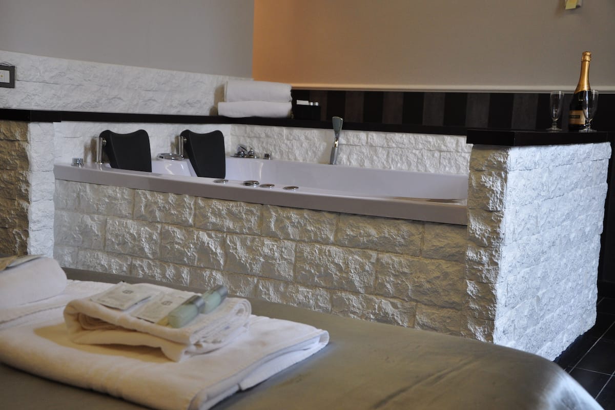 A bathroom with a stone wall, a white bathtub, a black towel, and a bottle of champagne.
