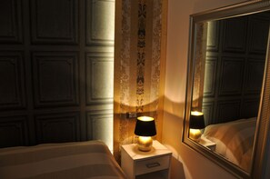 A hotel room with a bed, a nightstand with a lamp, a mirror, and a patterned wallpaper. - Navona Nice Room (Rome)