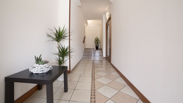 A hallway with a tiled floor, a black table with a plant, and a potted plant on the right. - Piccola Oasi (Vigonza)