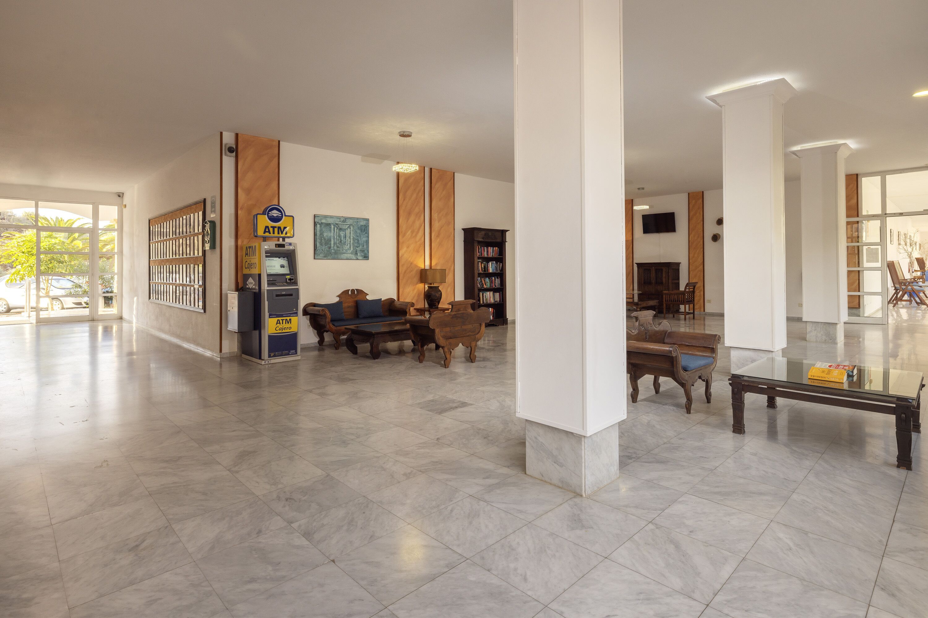A spacious lobby with a marble floor, a seating area with sofas and chairs, an ATM machine, and a bookshelf.