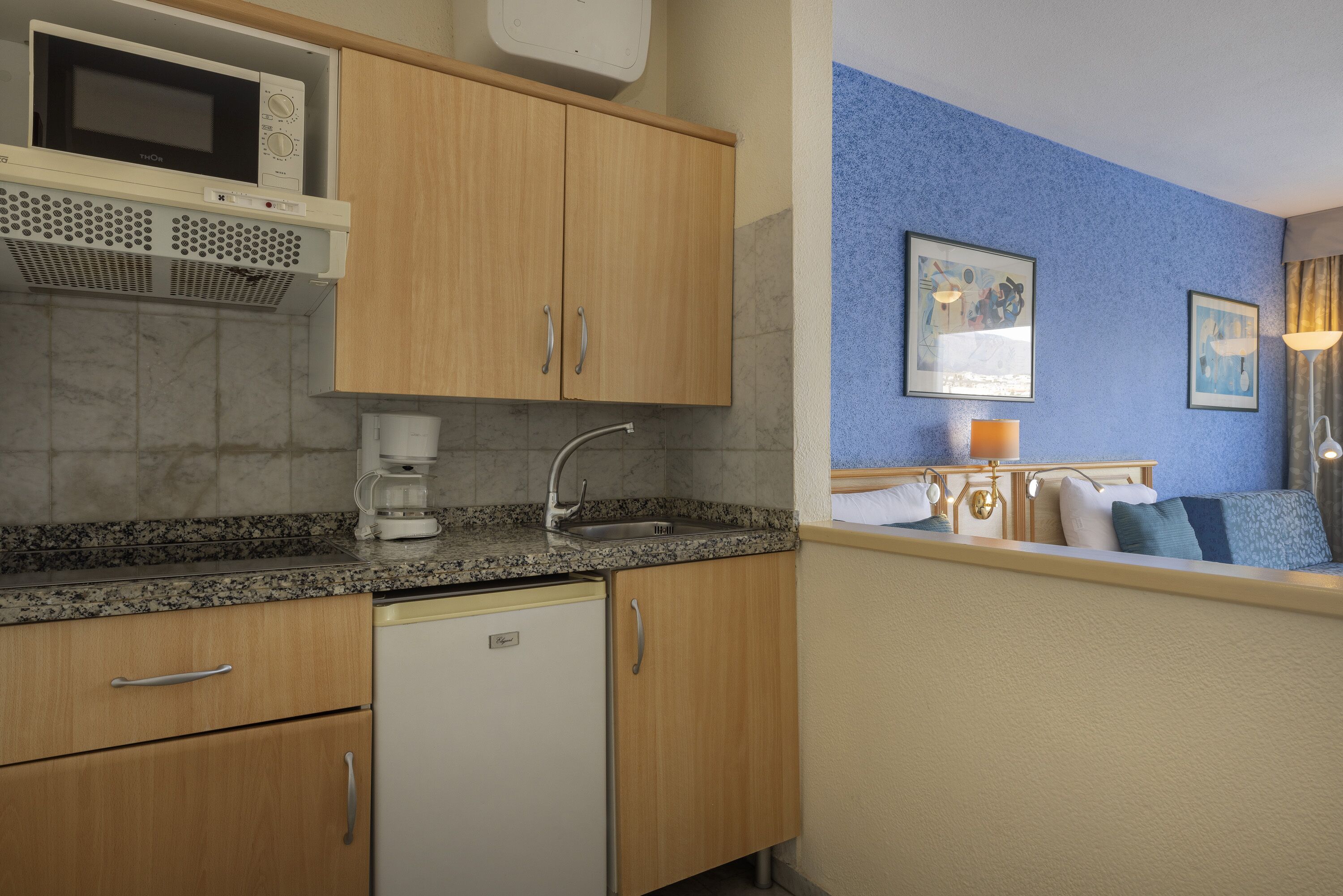 Una cocina compacta con armarios de madera, microondas, cafetera y pileta.